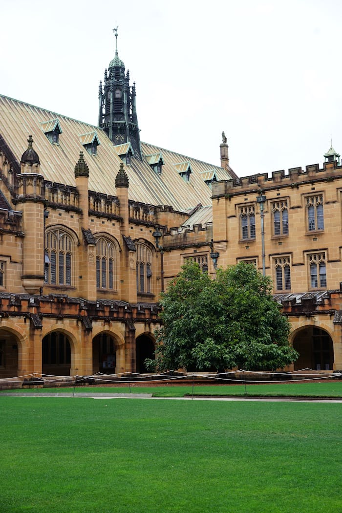 Gothic-style university building with a lush courtyard and green lawn.