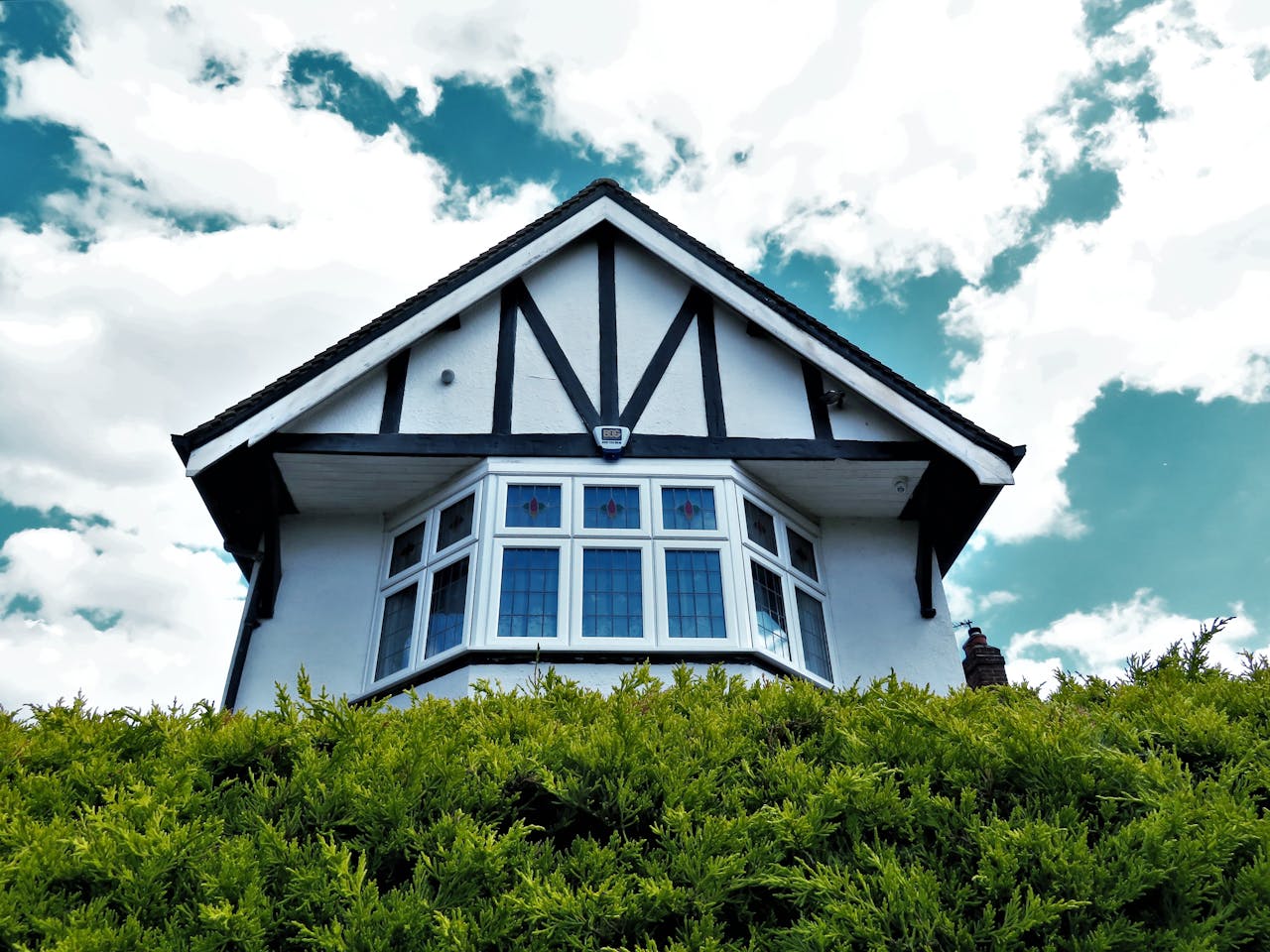 Tudor-style house facade with a bay window against a vibrant sky and greenery.